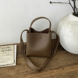 Brown litchi leather bucket bag with wide handle on wooden table near ceramic vase