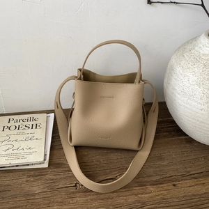 Minimalist khaki leather bucket bag with wide shoulder strap on a rustic wooden desk