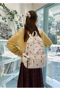 Detail view of cream backpack with red bow prints and a cute plush puppy pendant