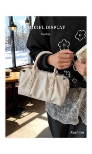 Detailansicht cremefarbene Plissee-Boston-Tasche mit Metallringen in gemütlichem Café