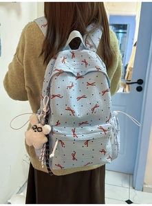 Detail of light blue backpack featuring red bow prints and a white rabbit plush charm