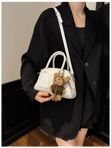 Detailaufnahme der weißen Croissant-Tasche mit Teddybär-Anhänger auf schwarzem Blazer
