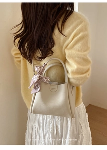 Detailansicht der beigen Eimer-Handtasche aus Leder mit lila Seidenschal und Markenetikett