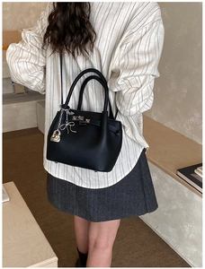Detail of black pebbled leather bucket bag with silver lock and bow pendant accessories