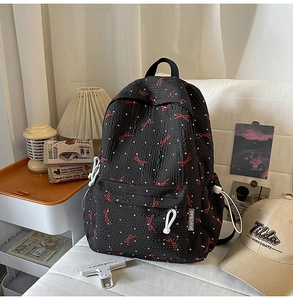 Detail of black backpack featuring red bows, white dots, and a round ring zipper pull