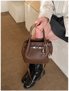 Detail of dark brown lychee texture leather handbag with silver lock and ribbon charm