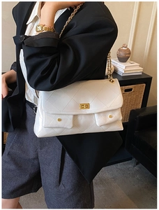 Detailed view of a white quilted tote bag with golden chain strap and shiny finish