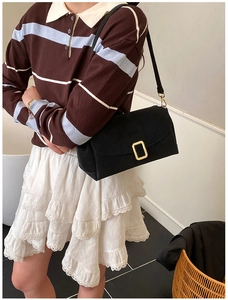 Détail d'un sac bandoulière rectangulaire noir avec boucle dorée porté par un mannequin