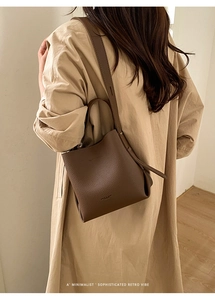 Detail of a brown lychee-pattern leather bucket bag featuring adjustable crossbody straps
