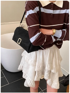 Détail d'un sac bandoulière carré noir mat avec boucle dorée sur un mannequin chic