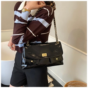 Close-up of black glossy quilted tote bag featuring golden twist lock and chain strap details