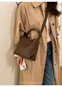 Brown lychee grain bucket bag with top handle and strap shown on beige trench coat