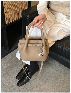 Detail view of khaki pebbled leather bucket bag with metallic charms and buckle on sofa