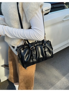 Detail einer schwarzen Falten-Boston-Tasche mit goldenen Ringen, getragen als Umhängetasche