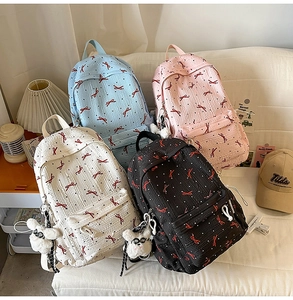 Detail view of colorful bow print backpacks in blue, pink, white, and black with plush charms