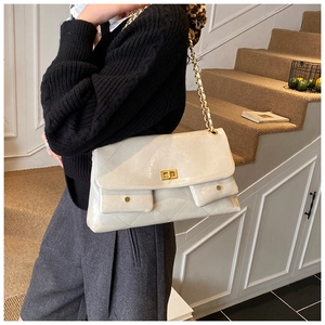Detail shot of a beige quilted shoulder bag with gold chain strap and dual front pockets