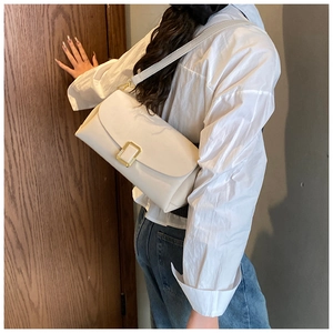 Détail d'un sac baguette minimaliste crème avec boucle dorée porté à l'épaule par un mannequin