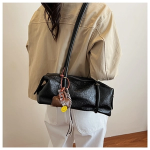Detail of black wrinkled patent leather shoulder bag with decorative bear charm and acrylic chain
