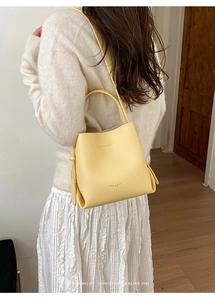 Chic light yellow bucket bag in lychee texture leather shown on a shoulder of a model