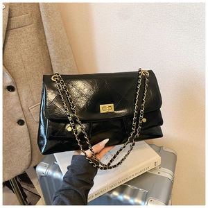 Detail of black quilted leather tote bag featuring a gold chain strap and metal lock closure