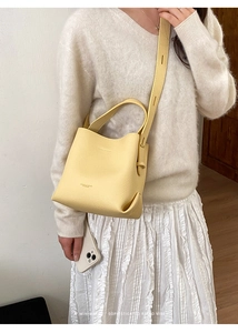 Detail of yellow lychee pattern leather bucket bag worn by model in minimalist setting