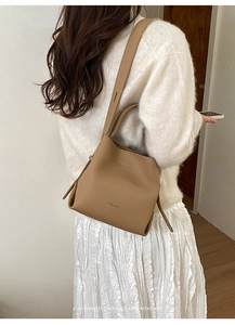 Close-up of brown litchi pattern leather bucket bag with wide shoulder strap on model