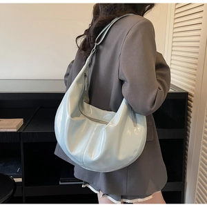 Detail of glossy patent leather dumpling bag in light blue on a stylish woman