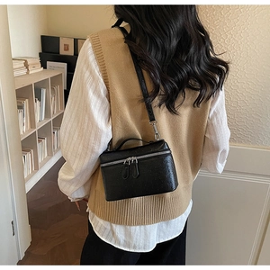 Detail view of black ostrich texture handbag with silver zippers and metal strap hooks