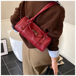 Detail of burgundy leather shoulder bag with gold metal clasp on a model in a minimal room