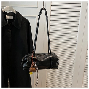 Detail of a black cylinder shoulder bag with glossy faux leather texture and charms