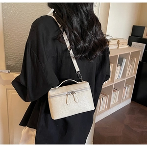 Detail of off-white ostrich embossed square bag worn crossbody in a vintage setting