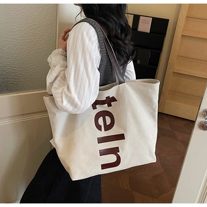 Détail d'un grand cabas en toile avec imprimé de lettres marron et longues anses en cuir
