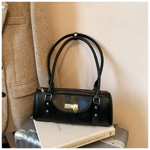 Detail of black cylindrical baguette bag featuring a metal heart pendant and slim straps