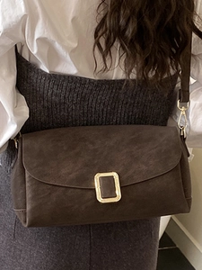 Sac bandoulière carré marron foncé avec boucle dorée porté par un mannequin