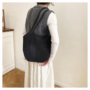 Detail view of black hand-crocheted hollow tote bag worn by a model in casual style