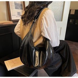 Detail view of glossy black faux leather shoulder bag with metallic buckle and wide strap