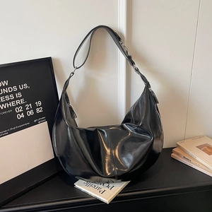 Detail of a large black glossy leather hobo bag with pleated texture and adjustable strap