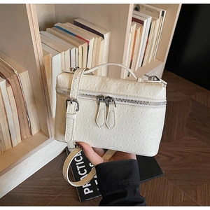 Detail of white ostrich-patterned box bag with silver zippers on a bookshelf