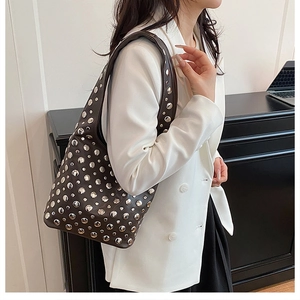 Close-up of a brown leather shoulder bag with silver metal studs worn by a model