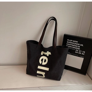 Détail du grand sac cabas en toile noire avec imprimé lettré et poignée en cuir marron