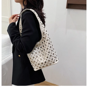 Close-up of a white shoulder bag featuring silver metal rivets and a wide strap design