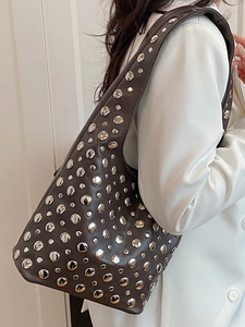 Brown leather underarm bag with silver rivets and punk style shown on a shoulder