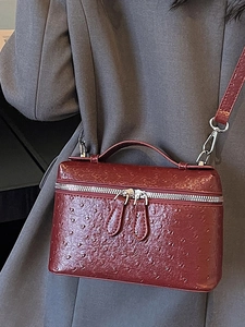 Elegant burgundy ostrich pattern box bag with silver hardware shown on a grey blazer