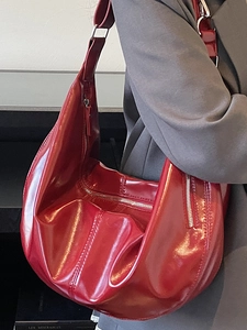 Glossy red hobo bag with zipper details and wide strap worn over a dark grey blazer