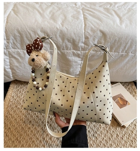 Detailed shot of cream polka dot shoulder bag featuring a cute plush bear charm and beads