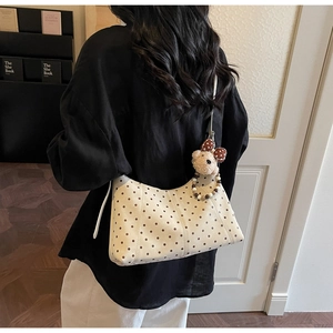 Polka dot canvas shoulder bag with plush bear charm worn by a model in a cozy room
