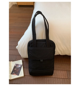 Macro shot of black quilted tote bag with front flap pocket and dual shoulder straps