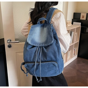 Rear view of a vintage washed blue denim backpack with drawstring closure on model