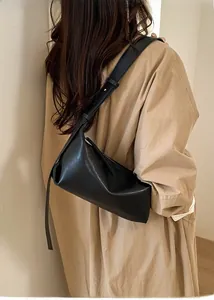 Detail view of a black minimalist leather crossbody bag worn with a stylish khaki trench coat