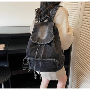Detail view of washed black denim backpack featuring drawstring closure and flap cover